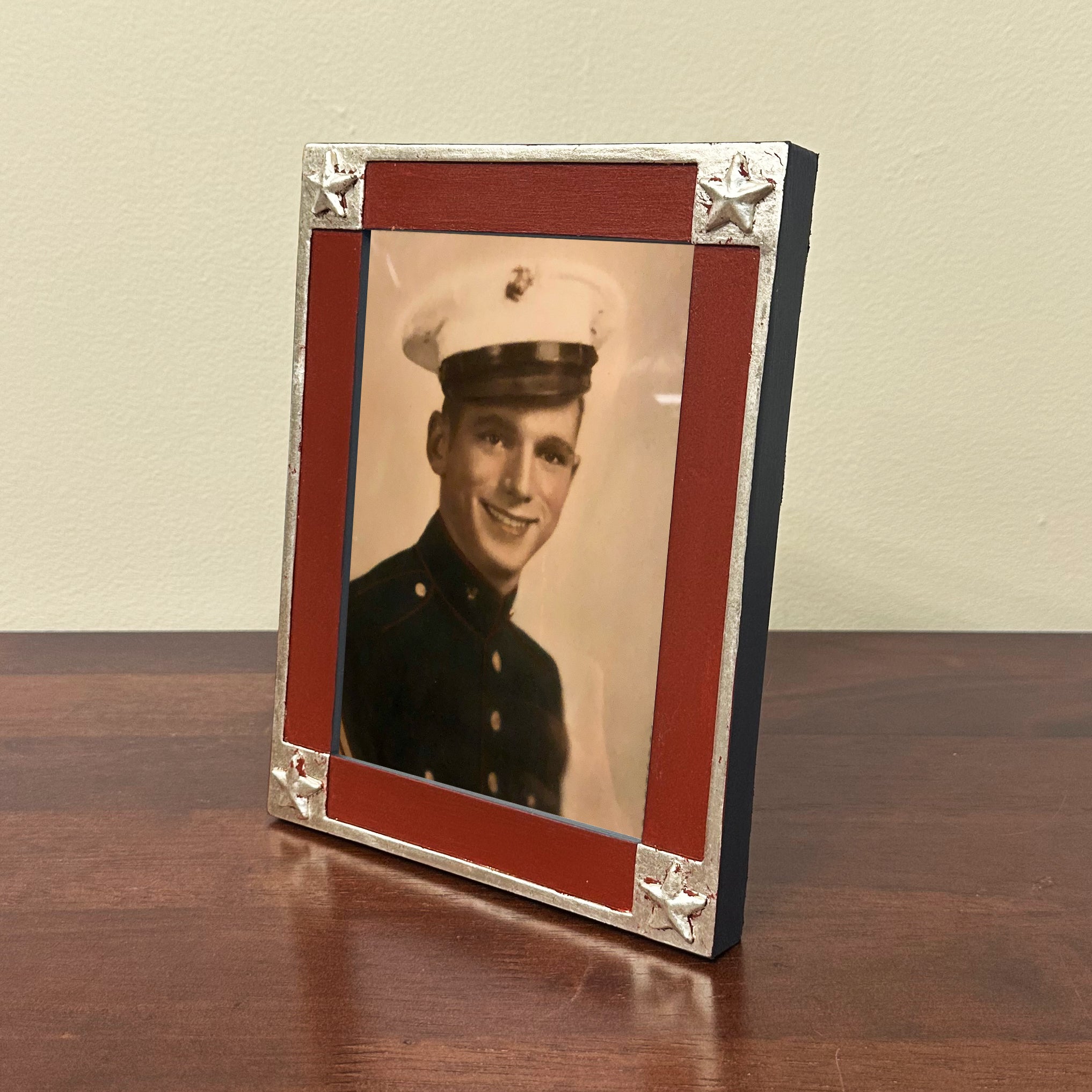 Vintage photo of a person in military uniform inside a decorative handmade frame on a wooden surface.